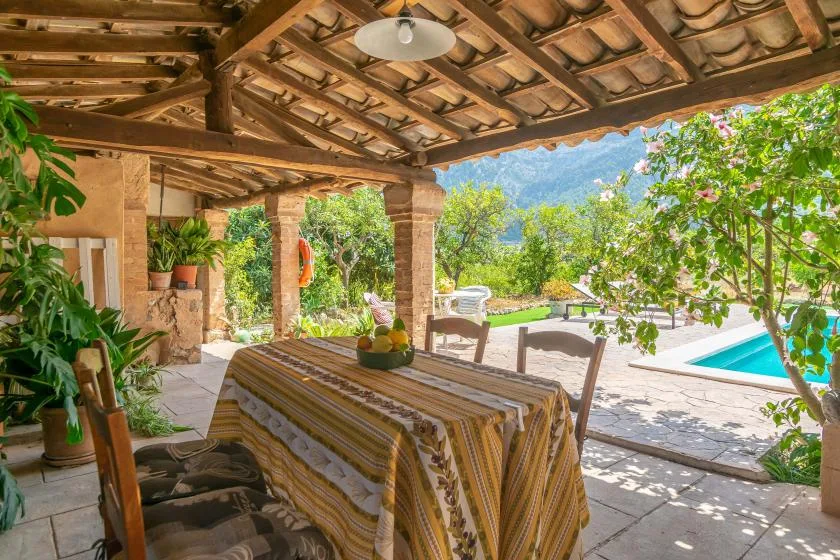 A covered outdoor dining area overlooks a pool and green landscape.