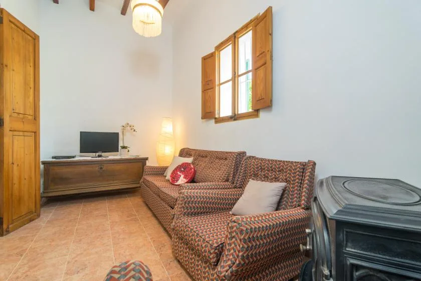 A bright living room with patterned seating, a wooden cabinet, and a window.