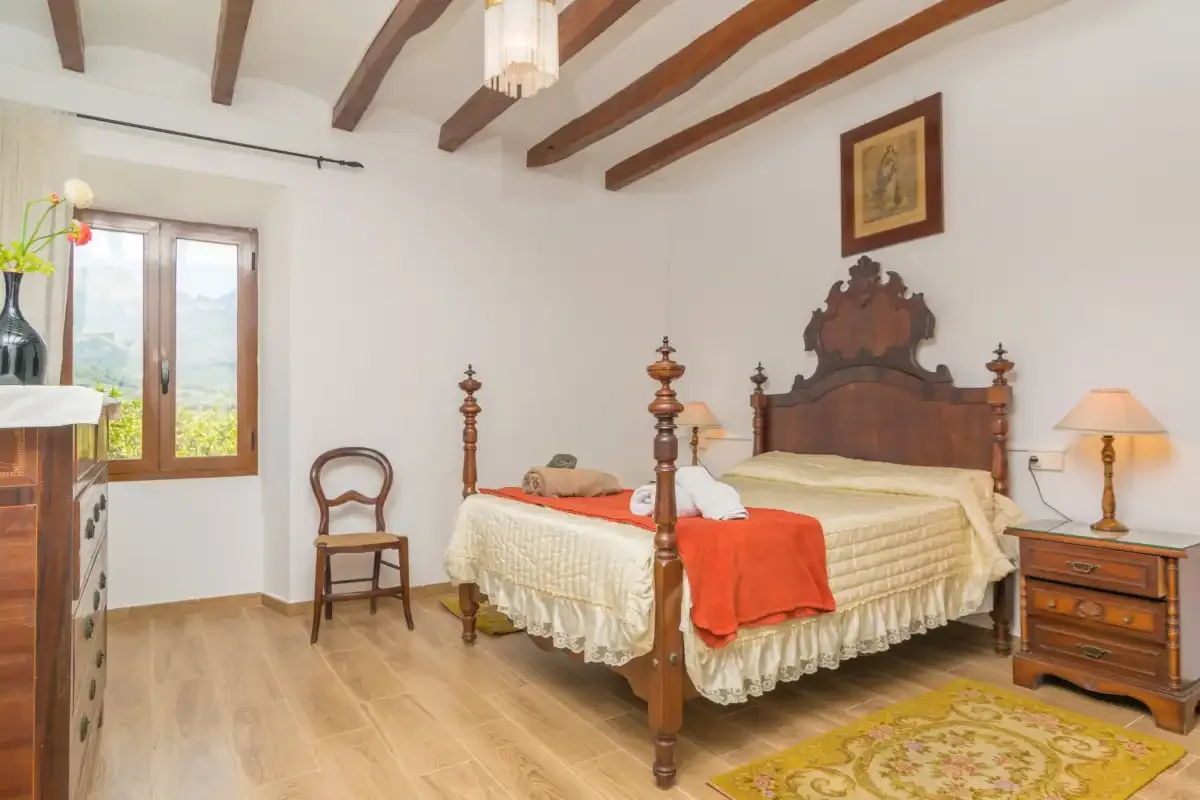 A bedroom with a wooden bed, a window, and exposed ceiling beams.
