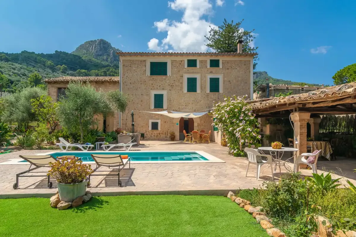 A stone house overlooks a swimming pool and garden patio.