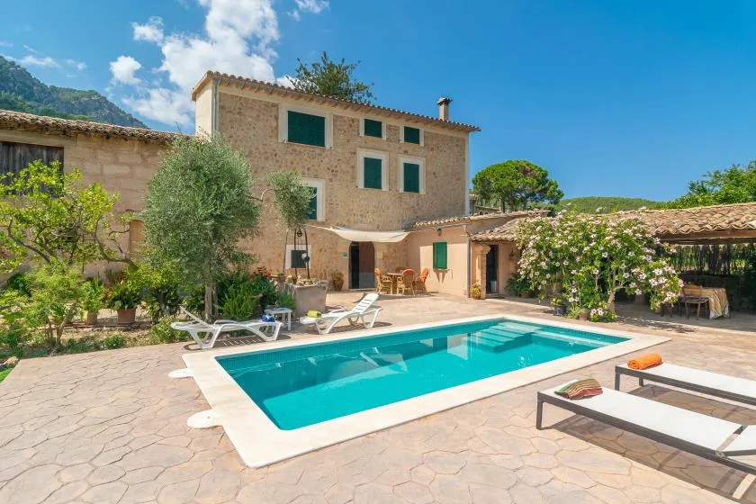 A stone house and outdoor swimming pool sit beside a sunny paved terrace.
