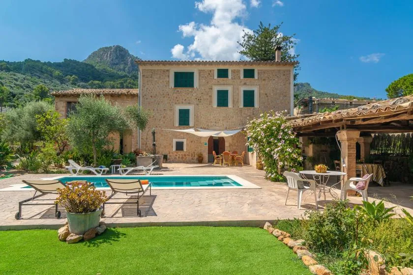 A stone house with a swimming pool, outdoor seating, and a green garden.