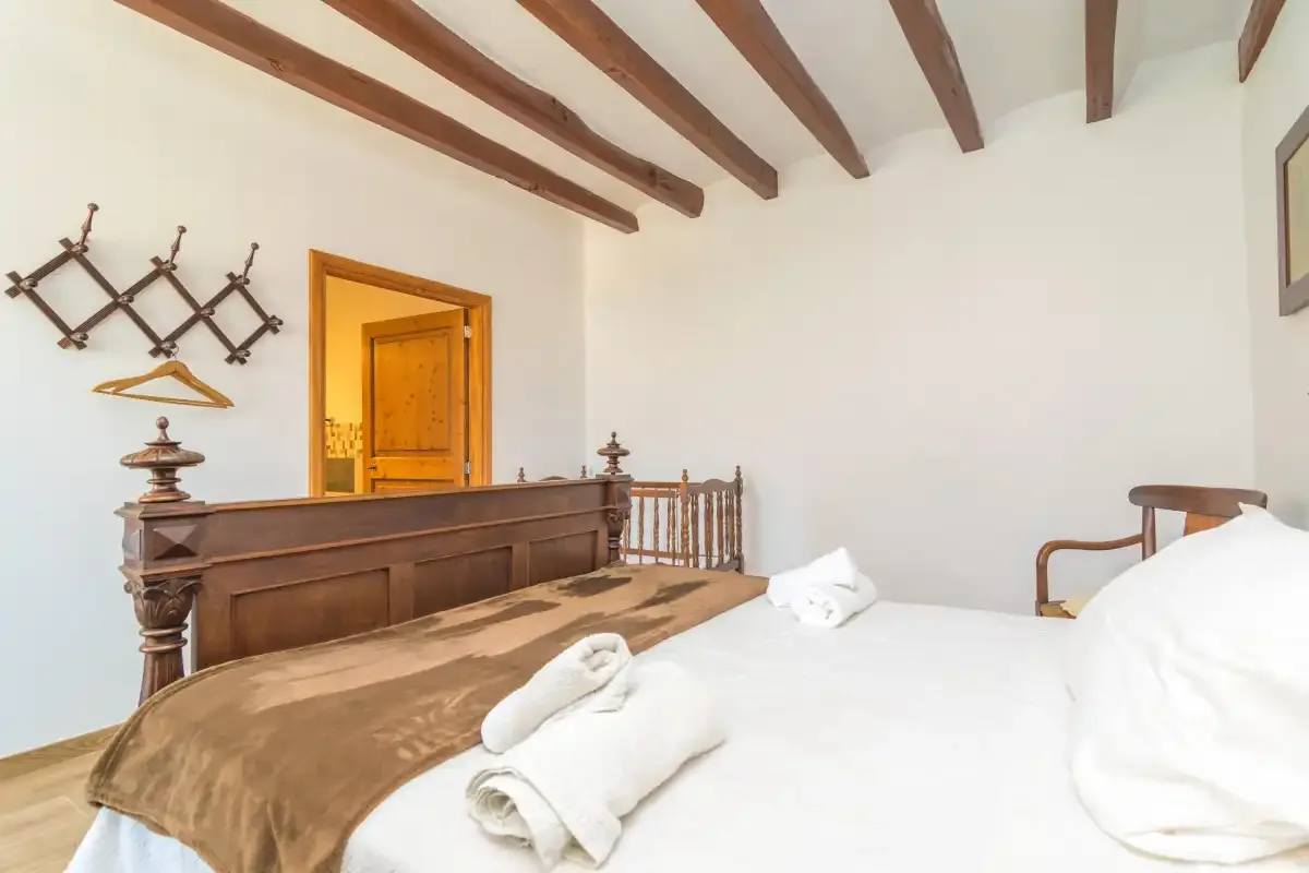 A bedroom with white bedding, folded towels, and exposed ceiling beams.
