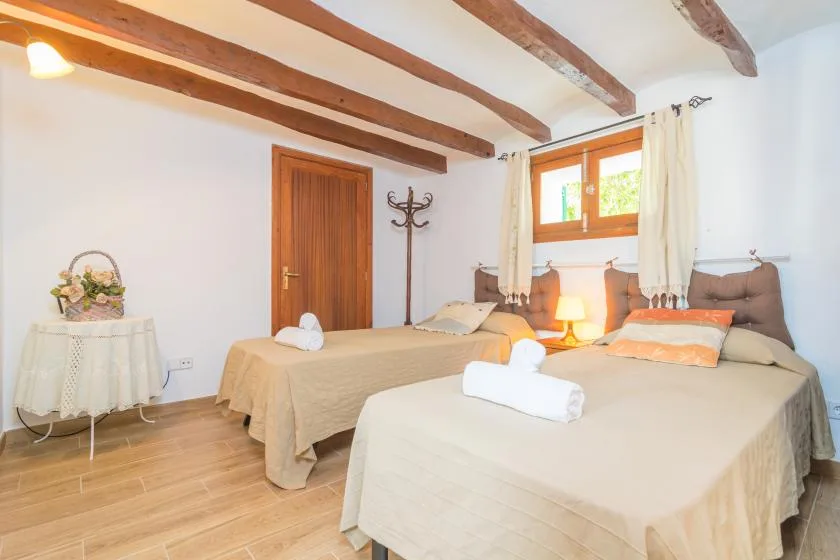 A bedroom with two beds, a small table, and exposed wooden ceiling beams.