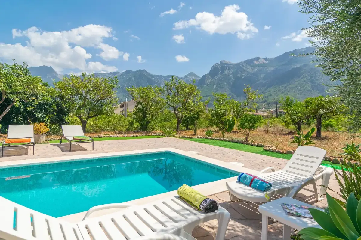 An outdoor swimming pool with lounge seating overlooks a tree-lined landscape and mountains.