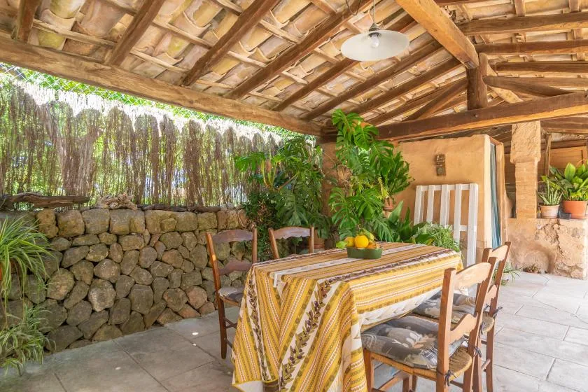 A covered outdoor dining area with a table, chairs, and leafy plants.