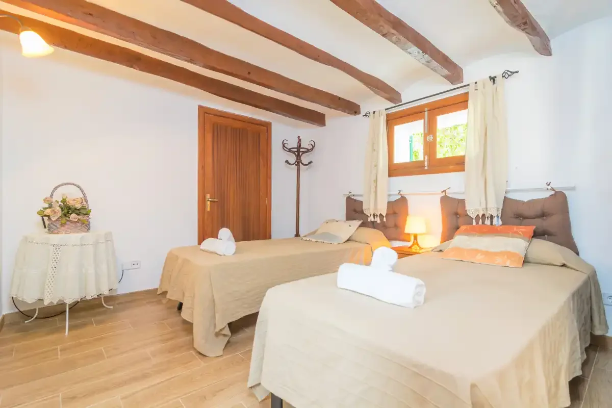 A bedroom with two beds, wooden ceiling beams, and a window.