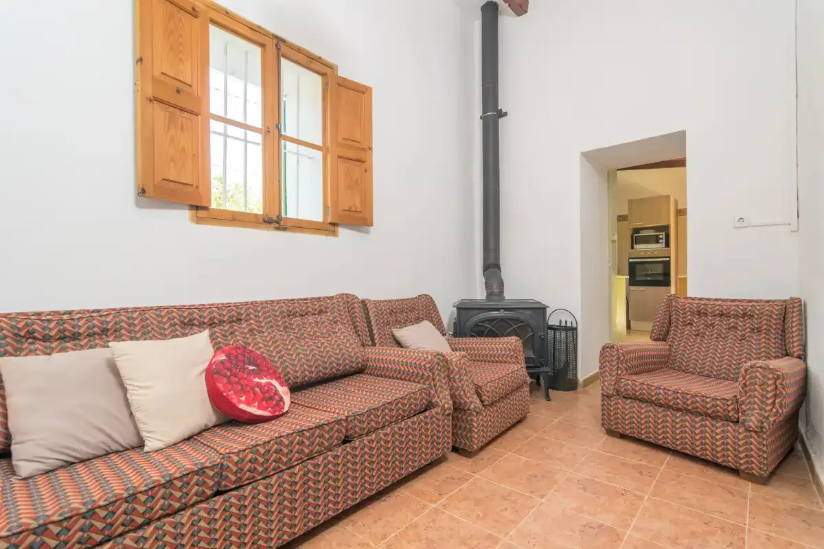 A living room with patterned seating, a wood-burning stove, and a window.