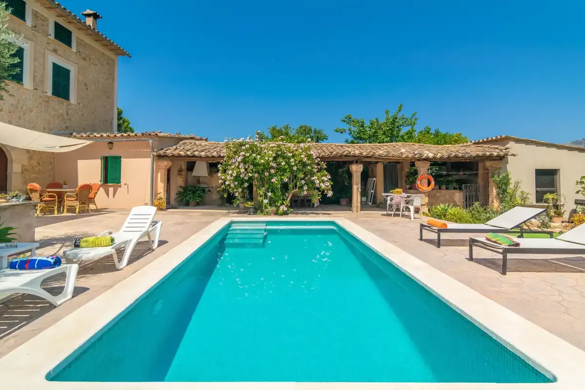 An outdoor swimming pool is surrounded by lounge seating and a tiled courtyard.