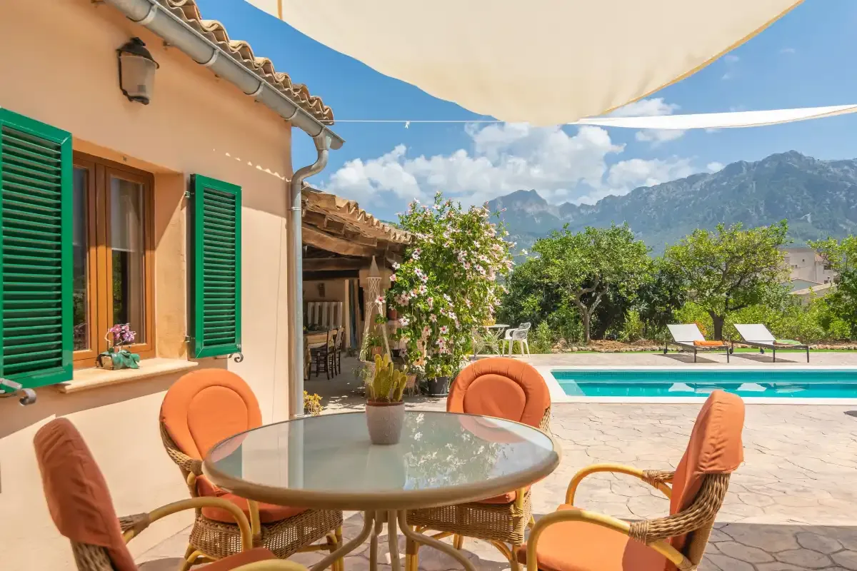 A shaded outdoor dining area overlooks a swimming pool and mountain scenery.