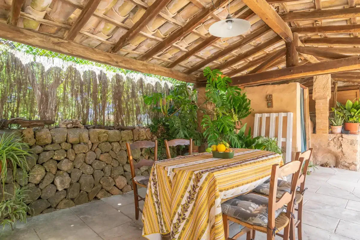 A covered outdoor dining area with a table and surrounding plants.