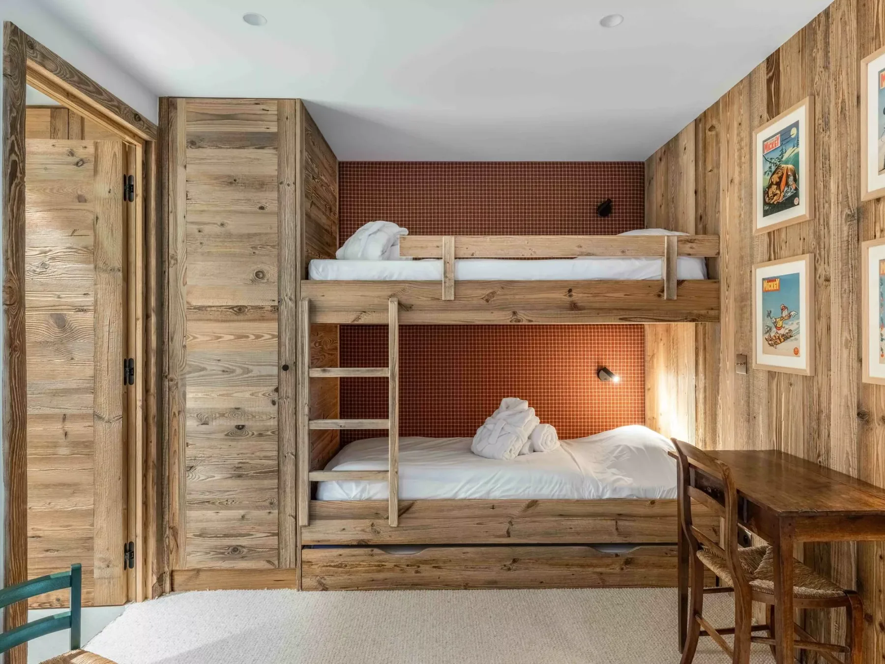 A wood-paneled bedroom with two bunk beds and a desk.