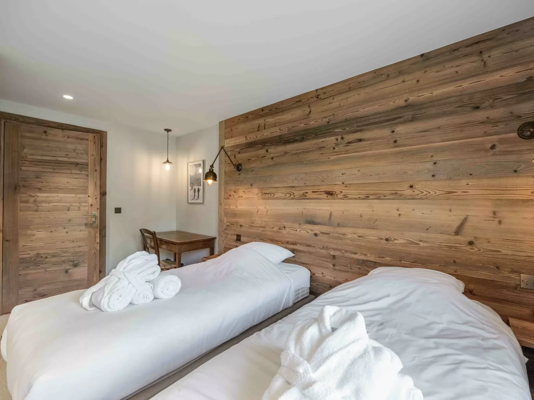 A bedroom with two beds, white linens, and a wood-paneled wall.