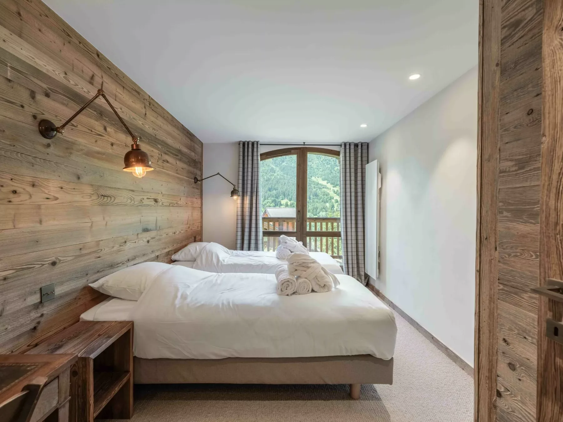 A bedroom with a bed facing a window and balcony.