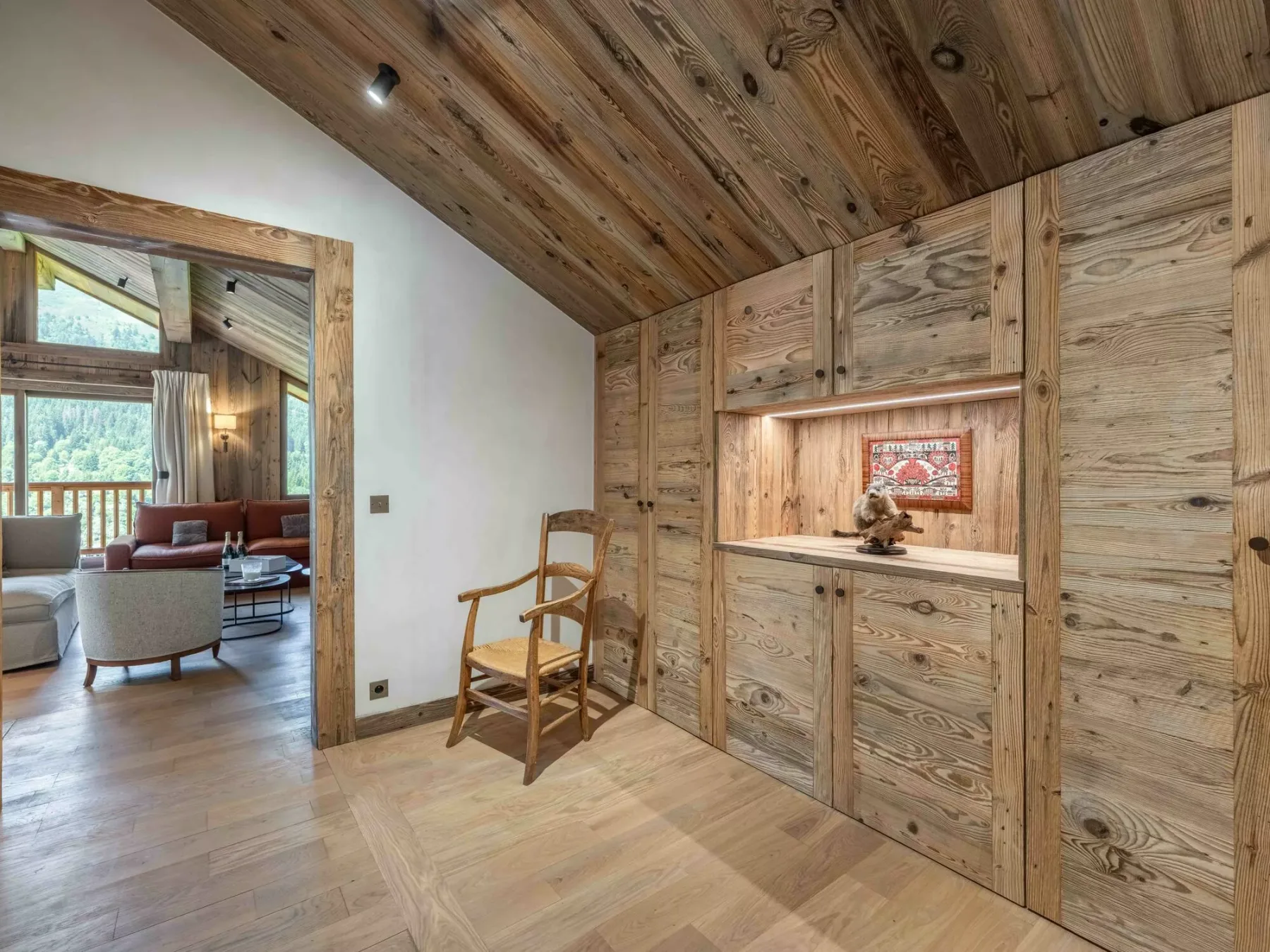A wood-paneled room with built-in cabinets and a chair beside an open doorway.