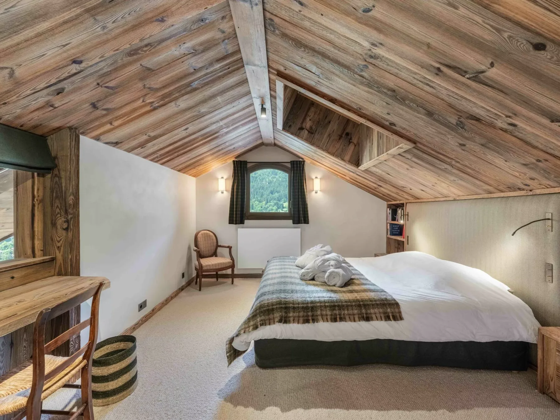 A bedroom with a bed beneath a sloped wood-paneled ceiling.