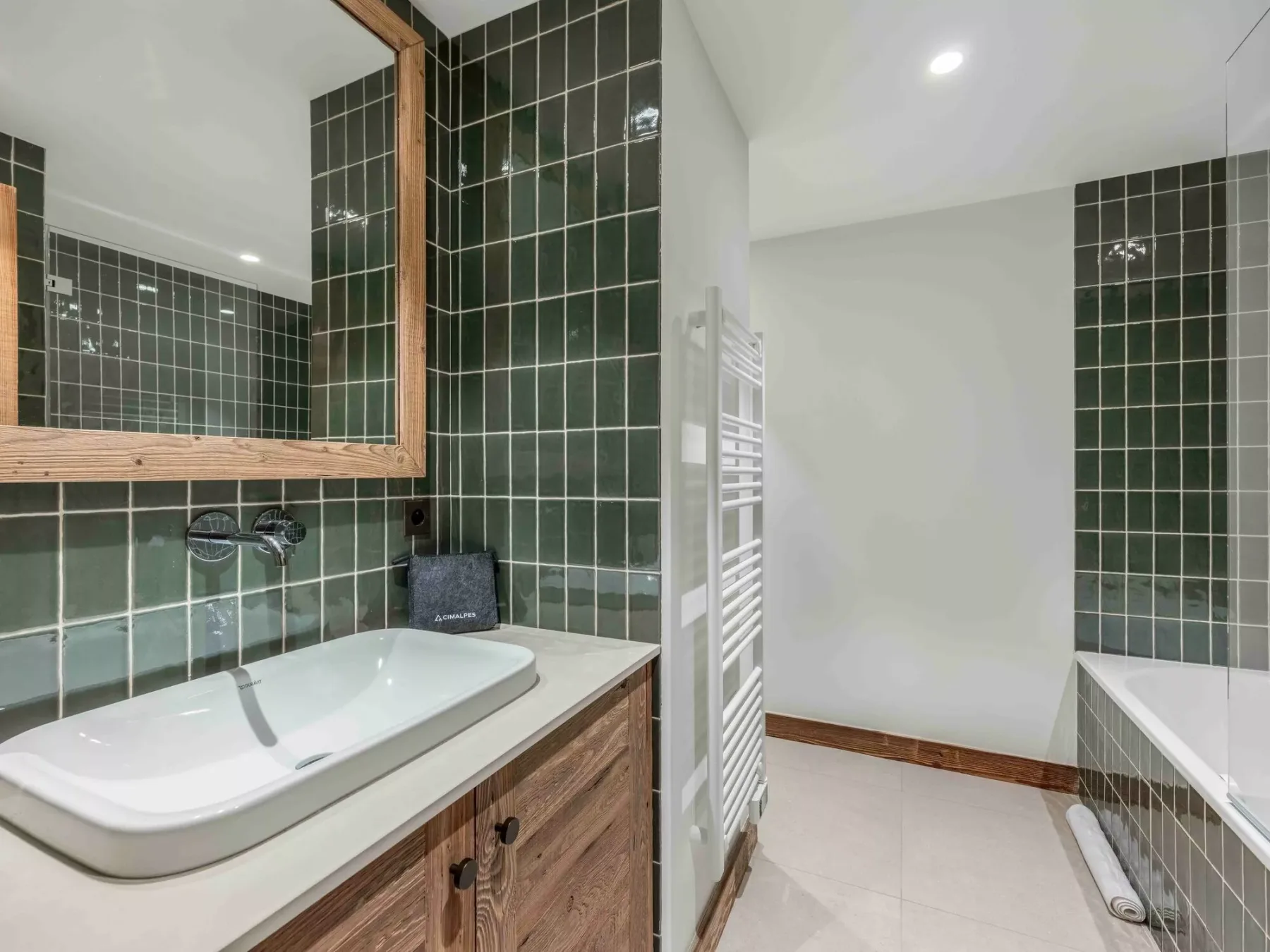 A tiled bathroom with a bathtub, vanity, and wall-mounted towel warmer.
