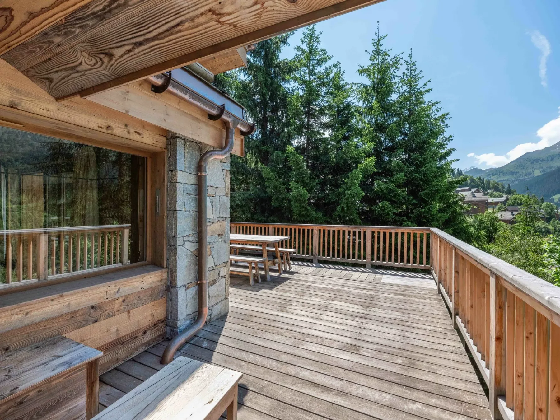 A wooden deck with railing and outdoor seating overlooks trees and mountain scenery.