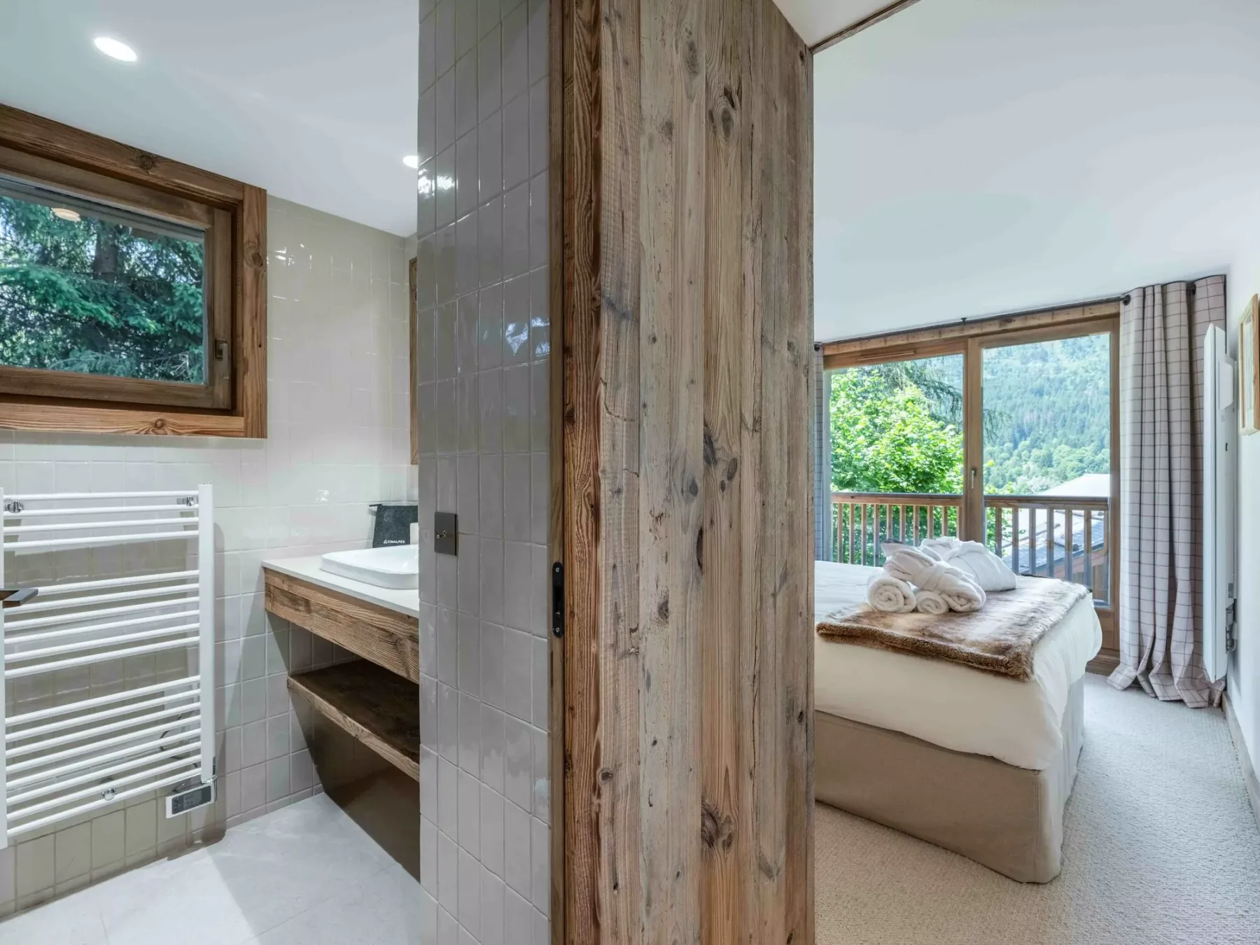 A bedroom with a bed beside large windows overlooking green hills.