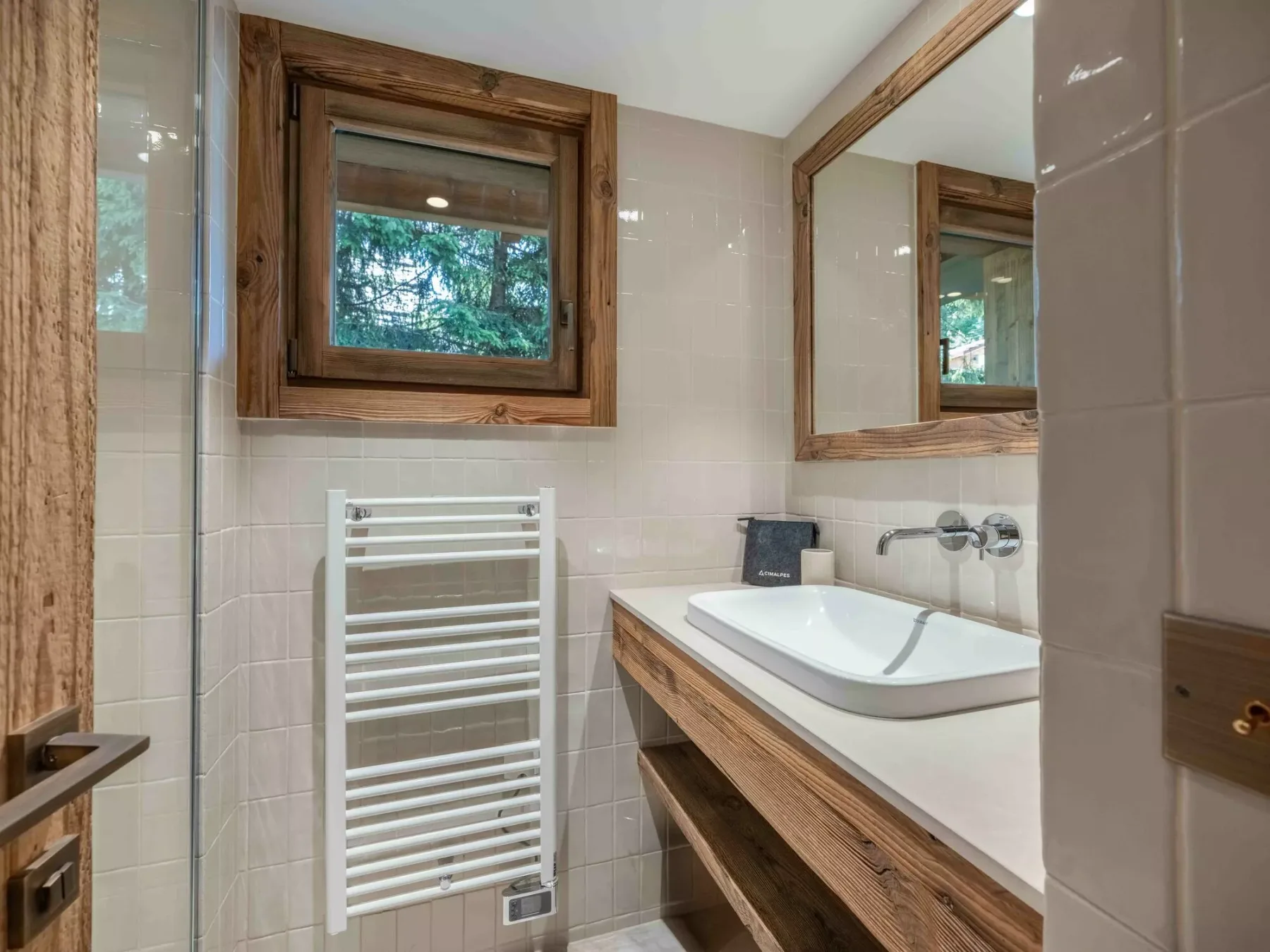 A tiled bathroom with a bathtub, wooden vanity, and window overlooking greenery.