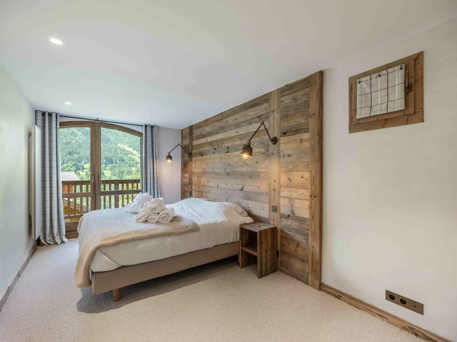 A bedroom with a bed beside a wooden plank wall and a balcony window.