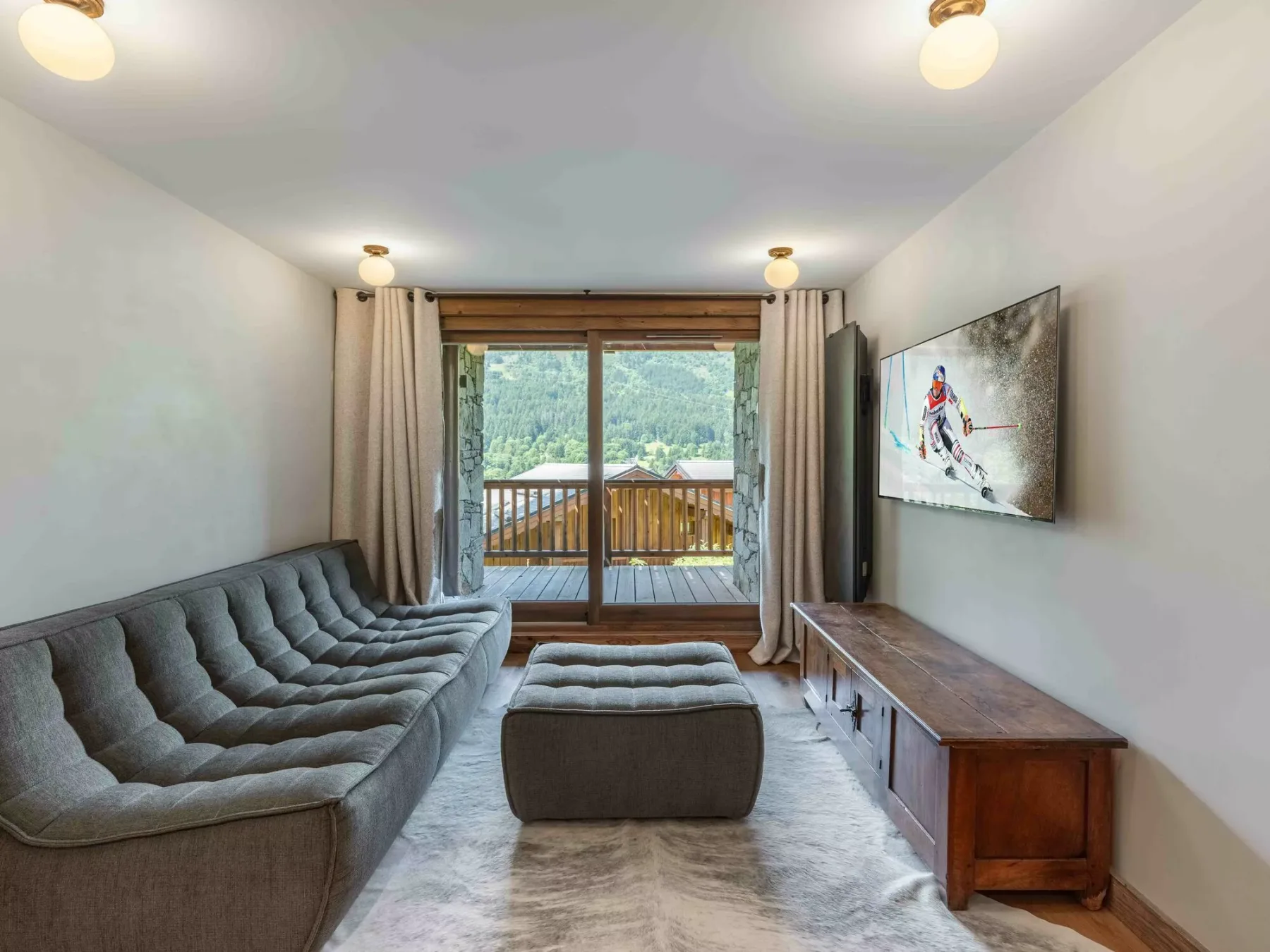 A living room with gray seating, a wooden media console, and glass doors opening to a balcony.