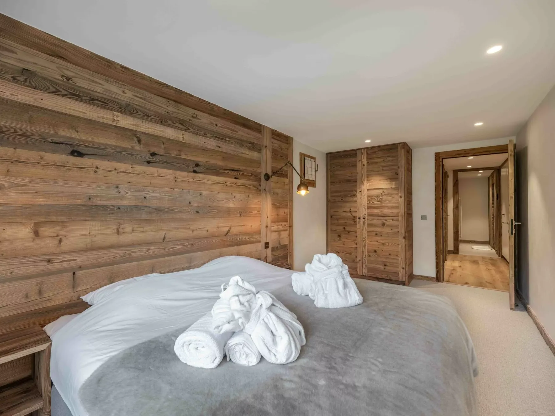 A bedroom with a bed dressed in white linens and wood-paneled walls.