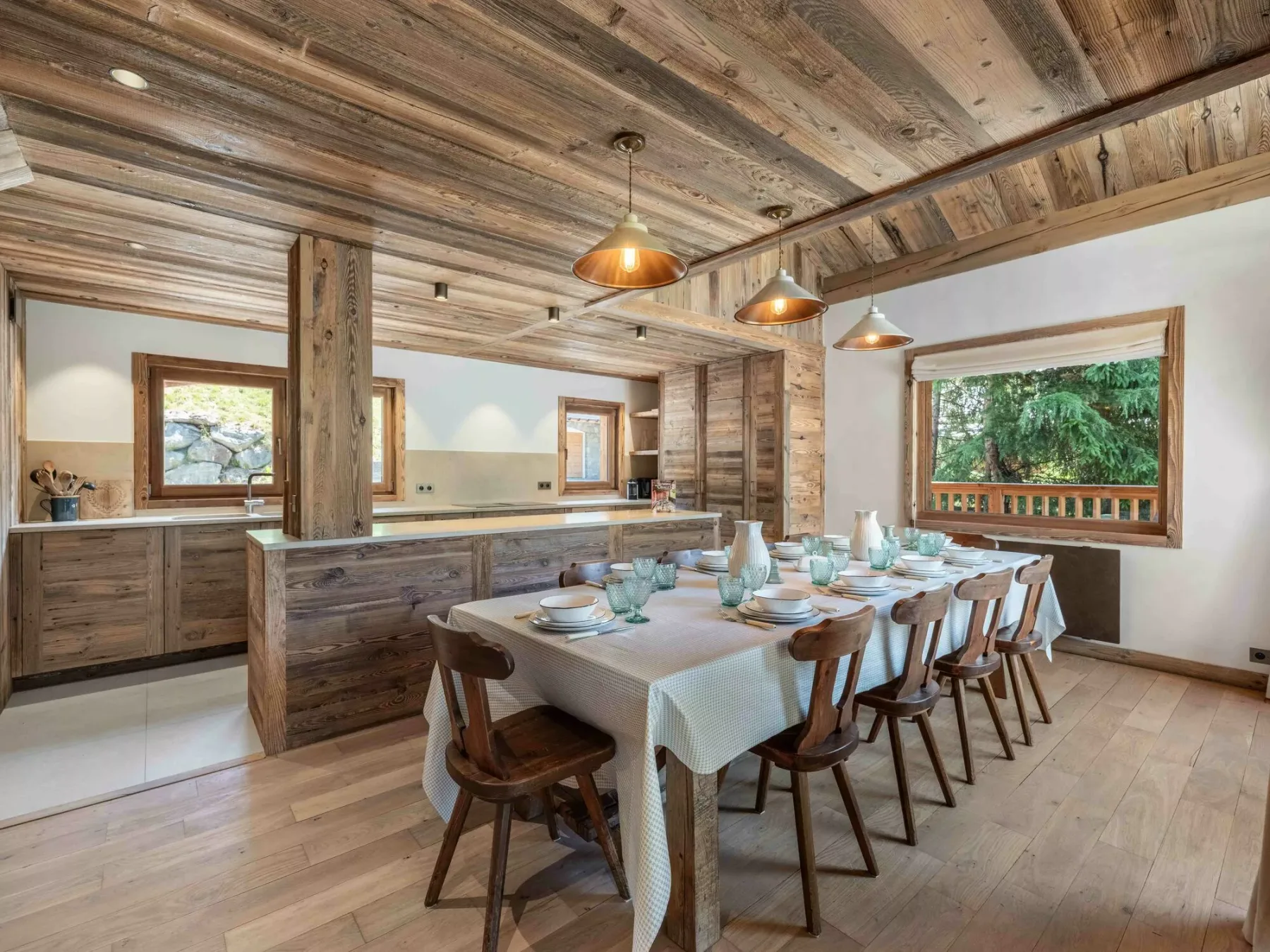 A rustic dining area with a long table set beside a wooden kitchen.