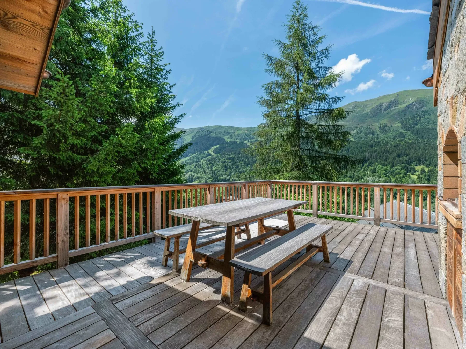 A wooden deck with picnic-style seating overlooks a forested mountain landscape.