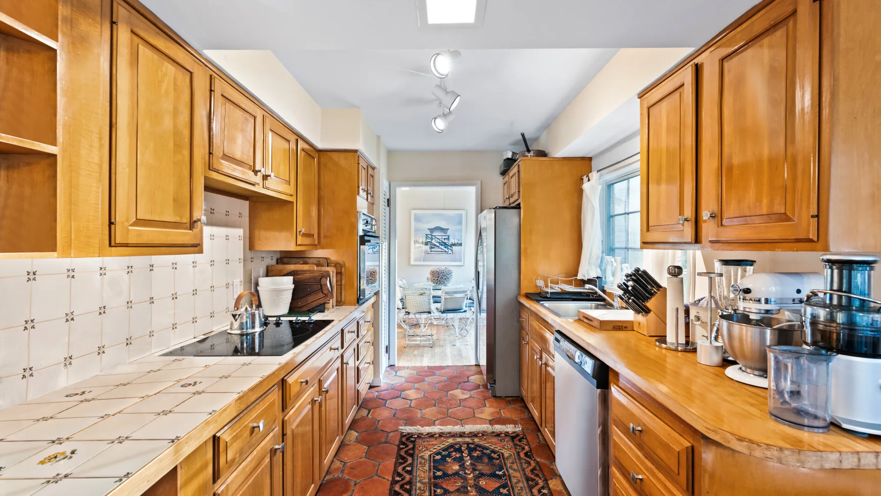 A narrow kitchen with wooden cabinets, tiled counters, and a patterned floor.