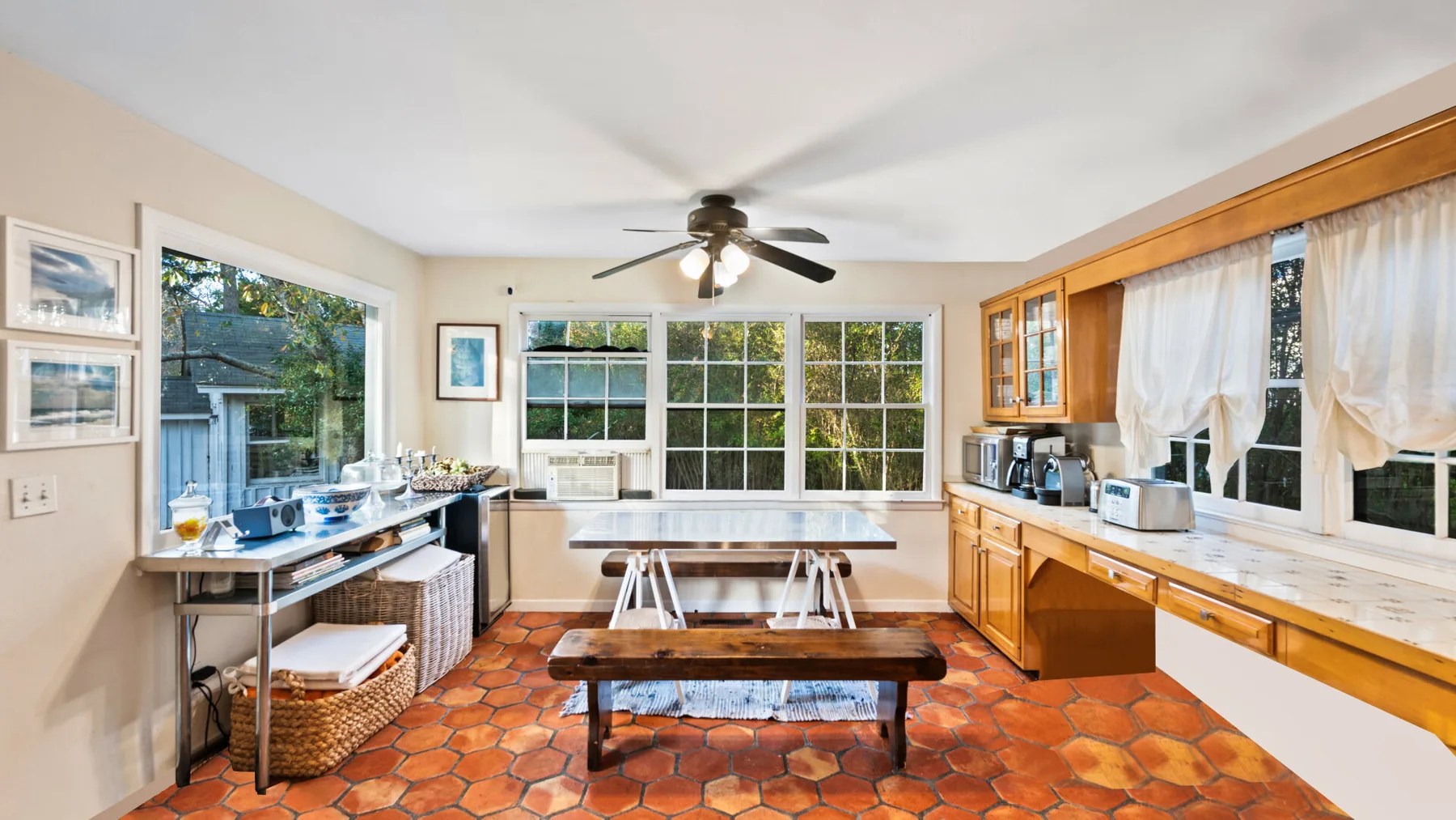 A bright kitchen and dining area with a long wooden table beneath large windows.