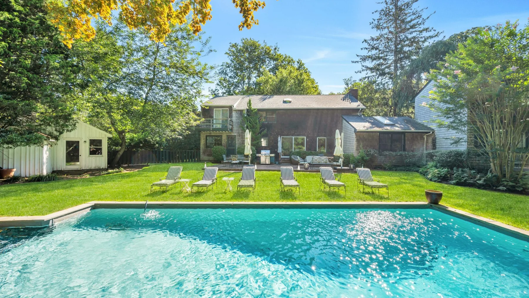 An outdoor swimming pool faces a landscaped lawn and a house.