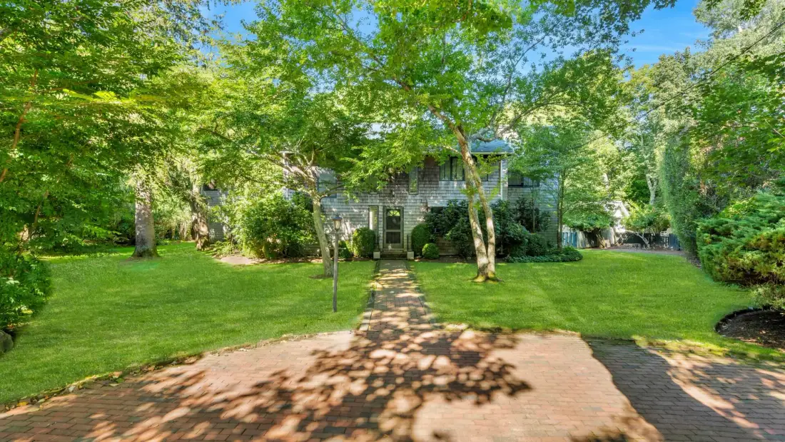 A tree-shaded garden path leads across a lawn toward a house.