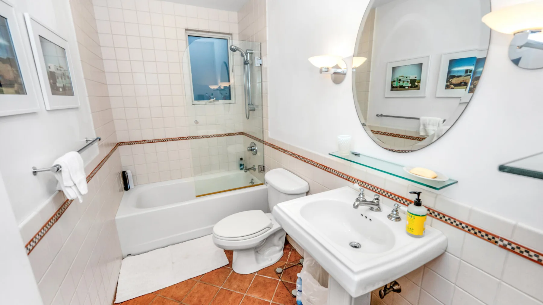 A tiled bathroom with a bathtub, toilet, and sink beneath a large mirror.