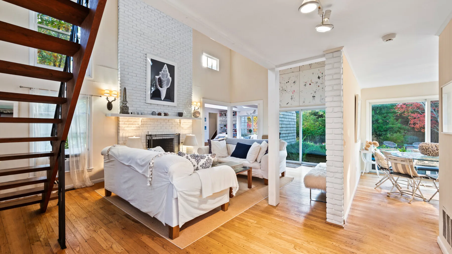 A bright living room with white seating and large windows opening onto greenery.