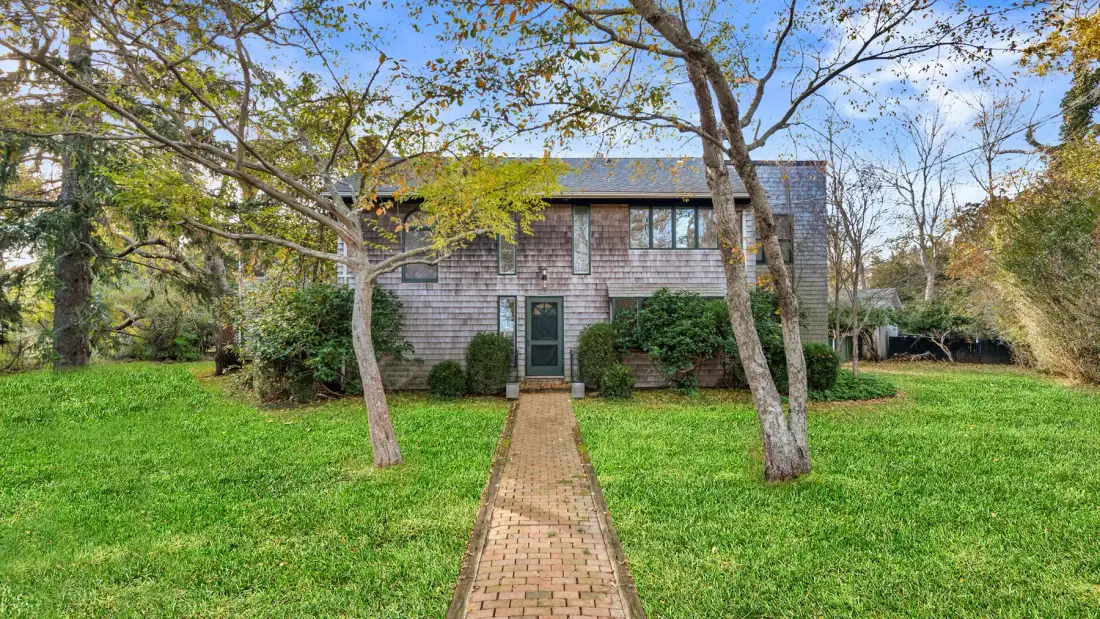 A two-story house stands beyond a brick path across a green lawn.