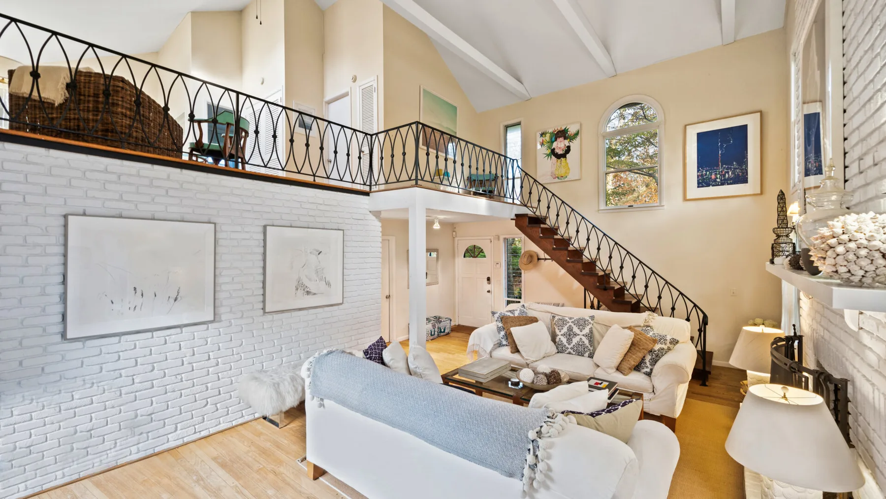 A bright living room with seating beneath a staircase and gallery railing.