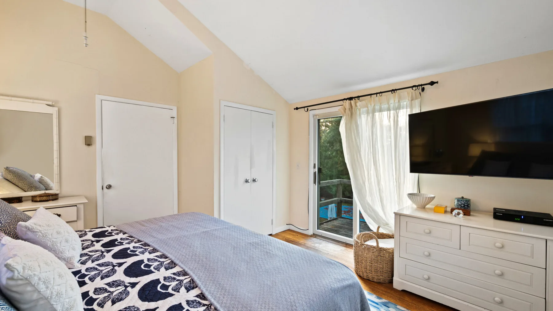 A bedroom with a bed, a dresser, and a television beside a curtained window.