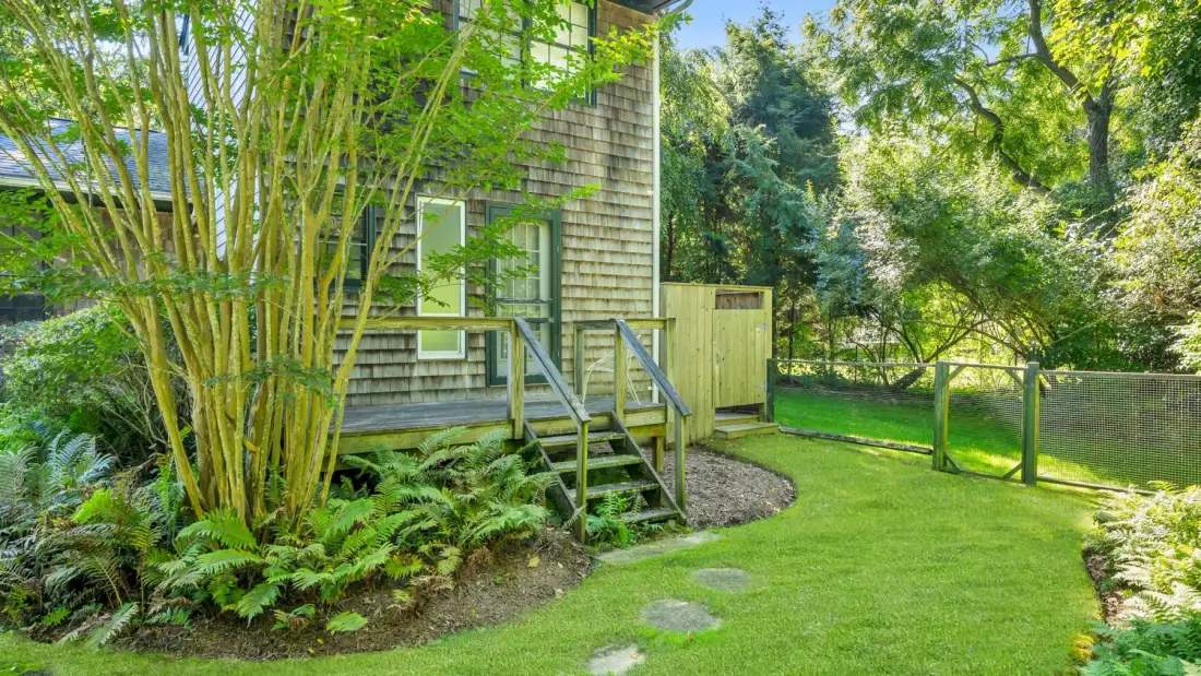 A garden path leads to steps beside a shingled house and green lawn.