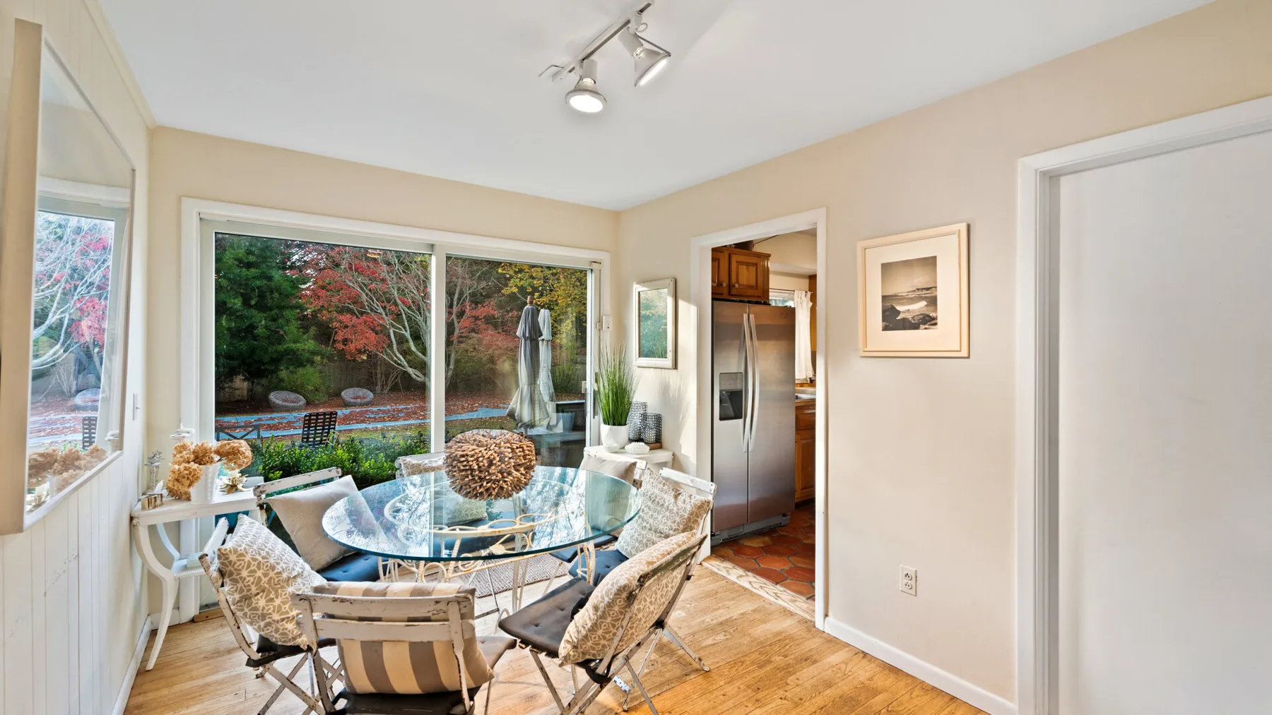 A bright dining area has a glass table and views of a garden.