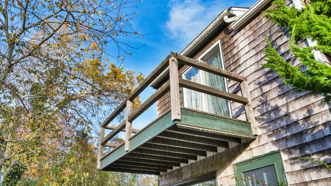 A small wooden balcony projects from the side of a shingled house.