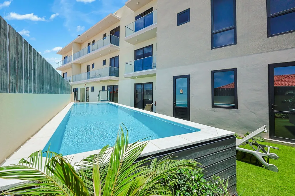 A stylish modern residence with sleek glass-railed balconies and a sparkling lap pool surrounded by a bright, sun-filled courtyard.