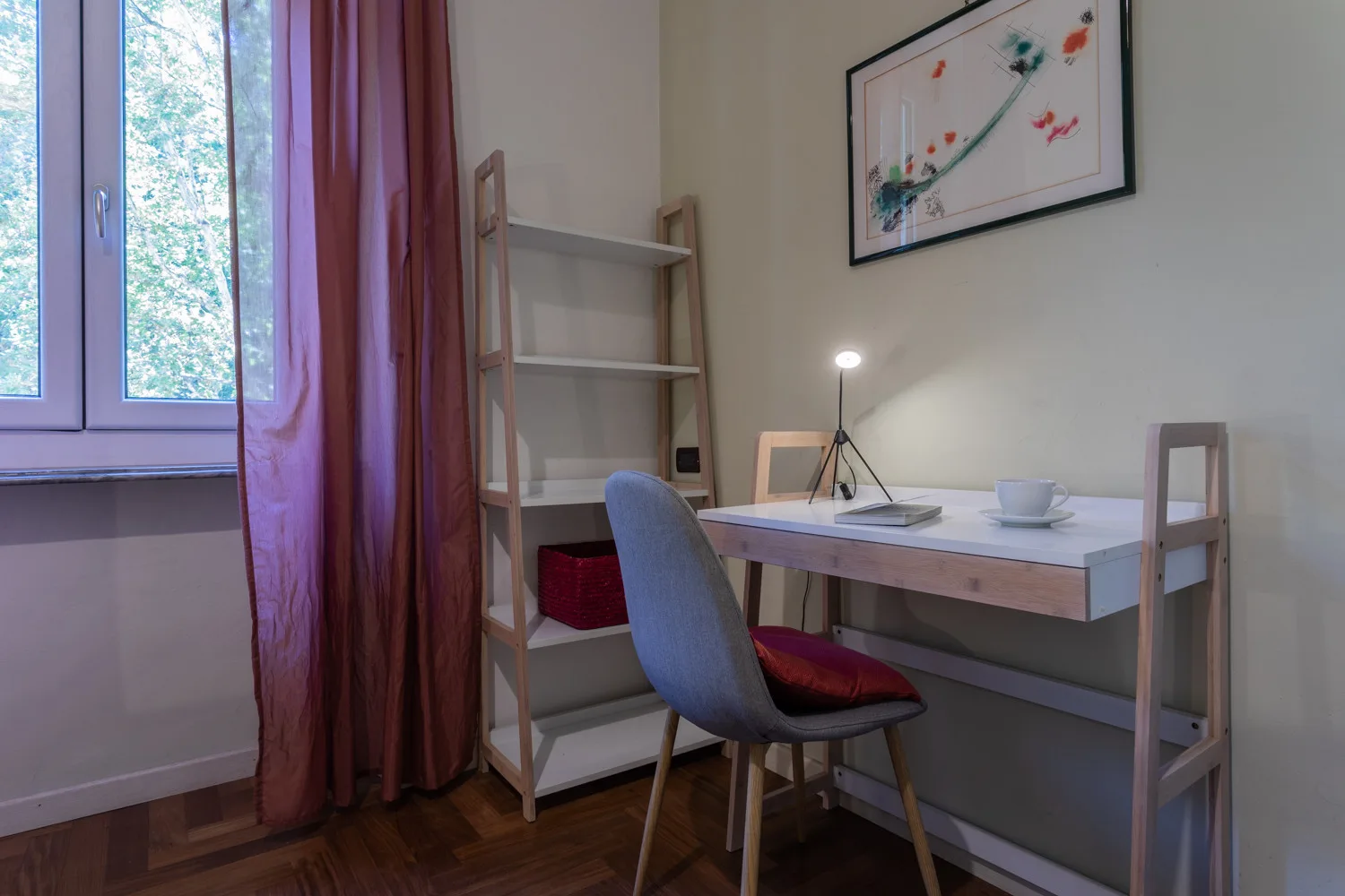 A study area with a desk, chair, and shelving beside a window.