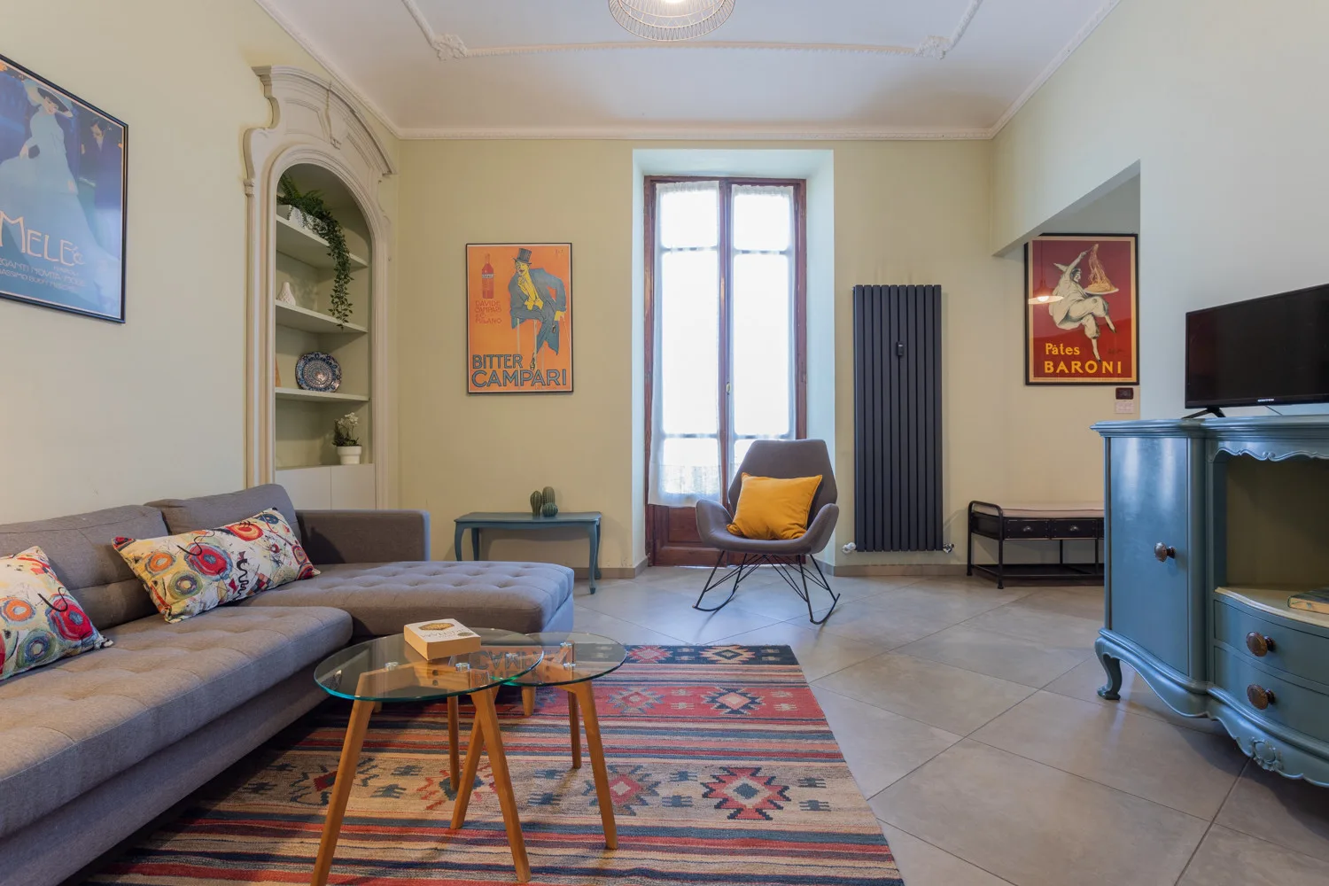 A living room with seating, a patterned rug, and a tall window.