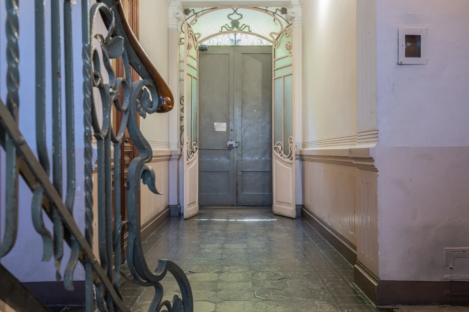 A hallway with ornate open doors leading to a closed gray door.