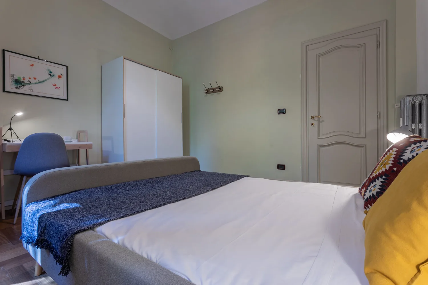 A bedroom with a bed, a desk, and a white wardrobe.