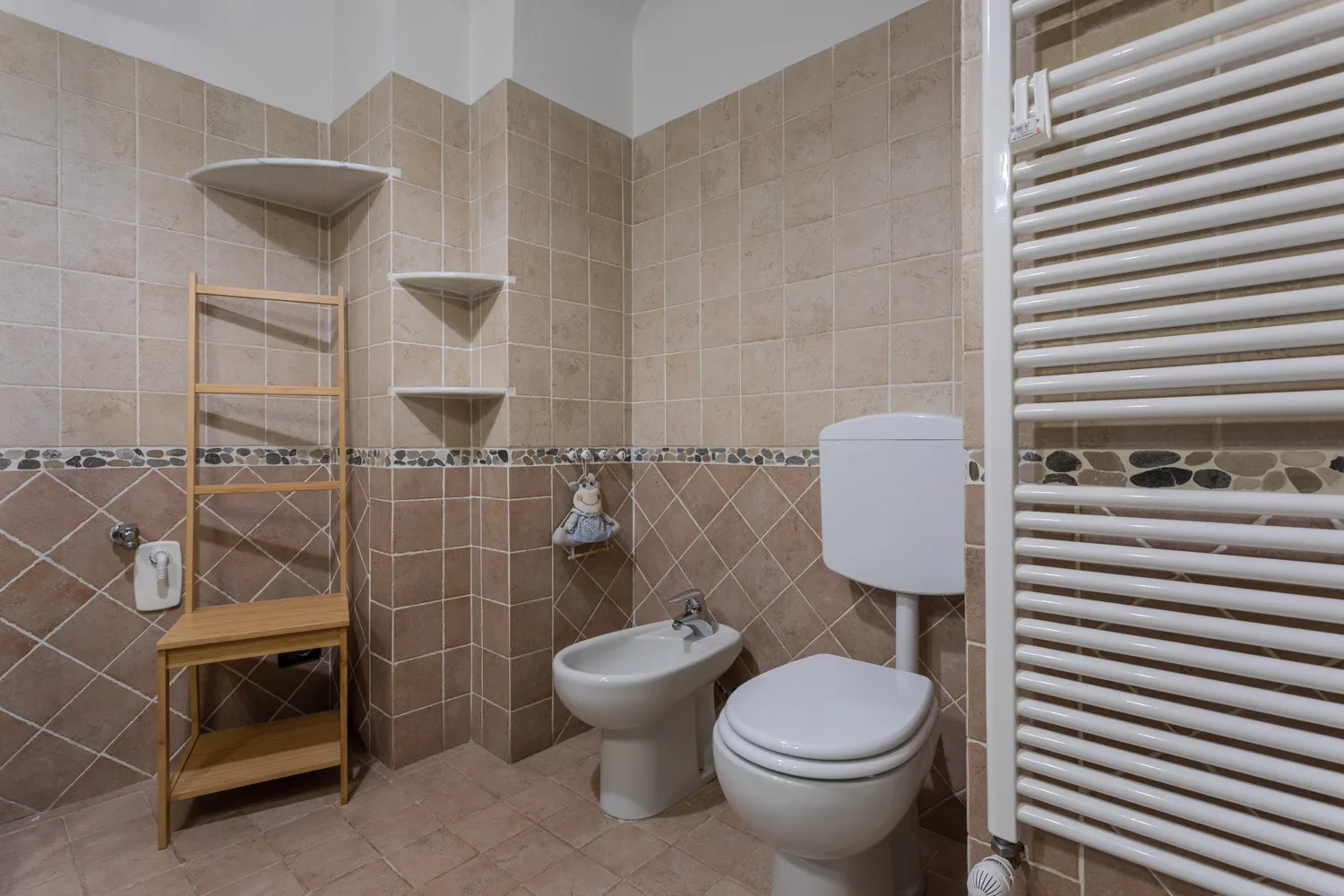 A tiled bathroom with a toilet, bidet, and wall-mounted radiator.
