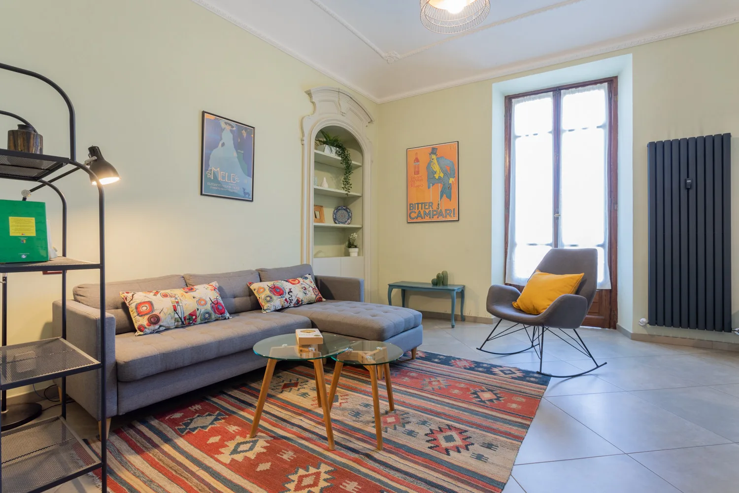 A living room with seating, a patterned rug, and a tall window.