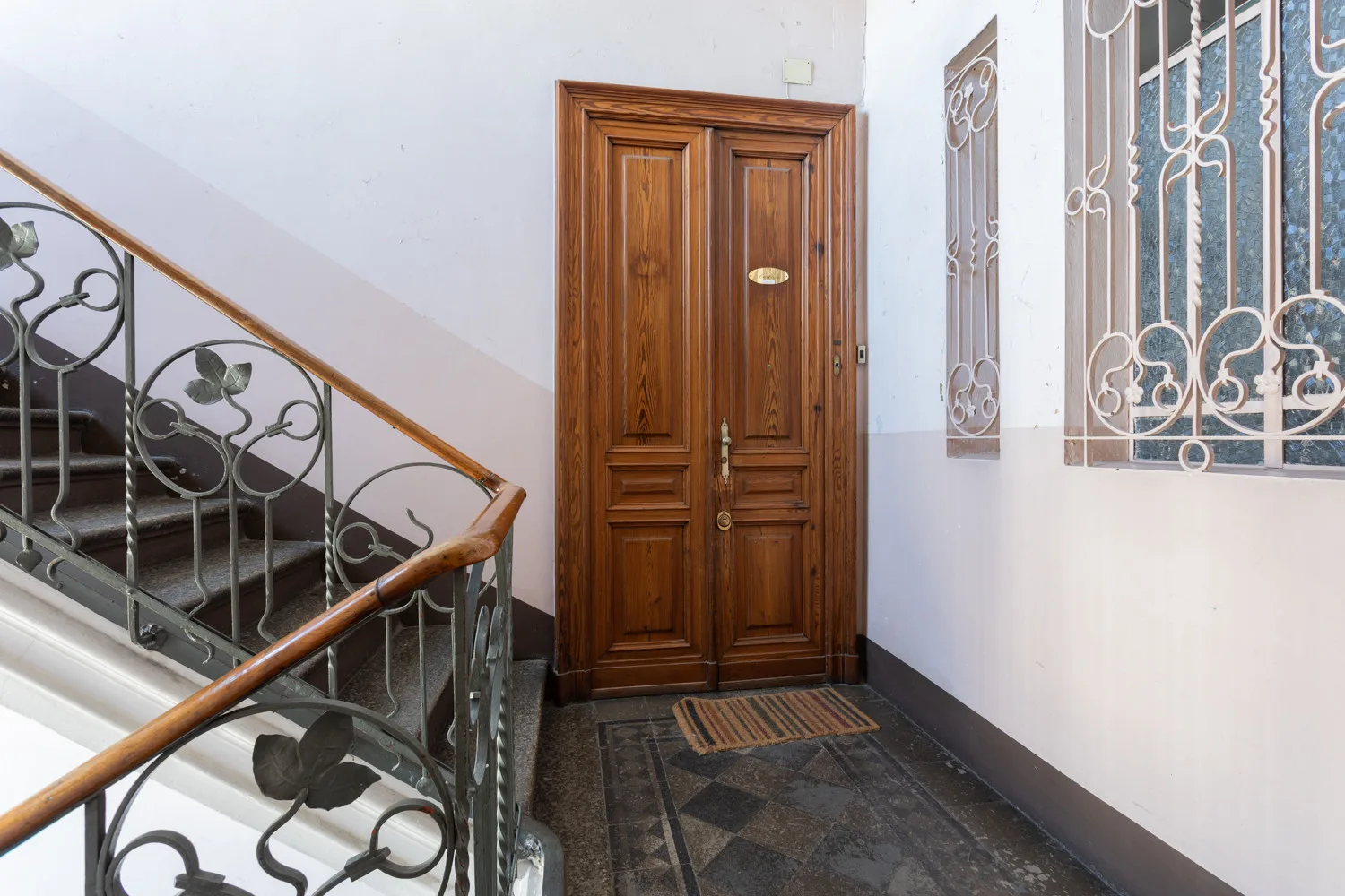 A stairwell landing with a wooden door and a decorative metal railing.