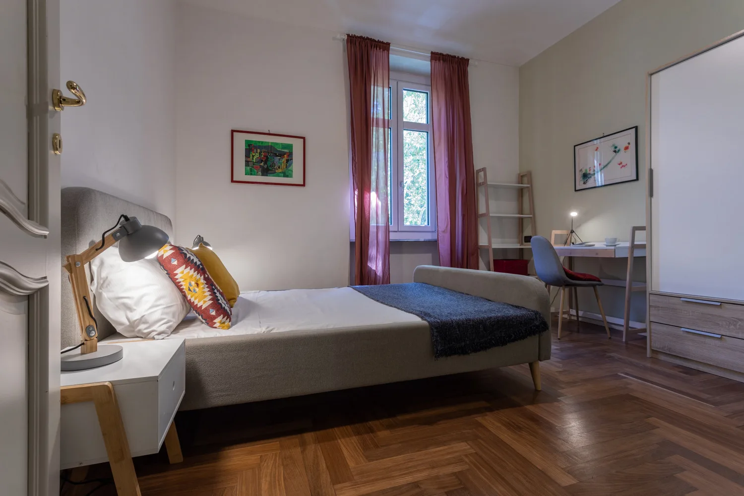 A bedroom with a bed, a desk, and a window with curtains.